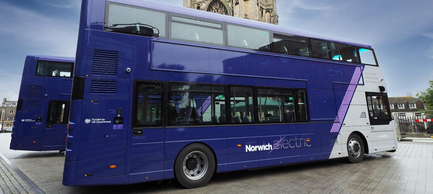 purple and grey double decker bus parked in front of a tower with stormy sky in the background