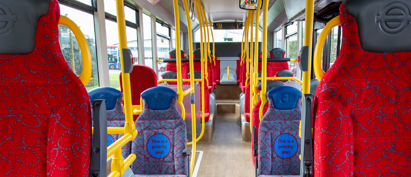 single deck bus interior showing red and grey high back seats and yellow handrails