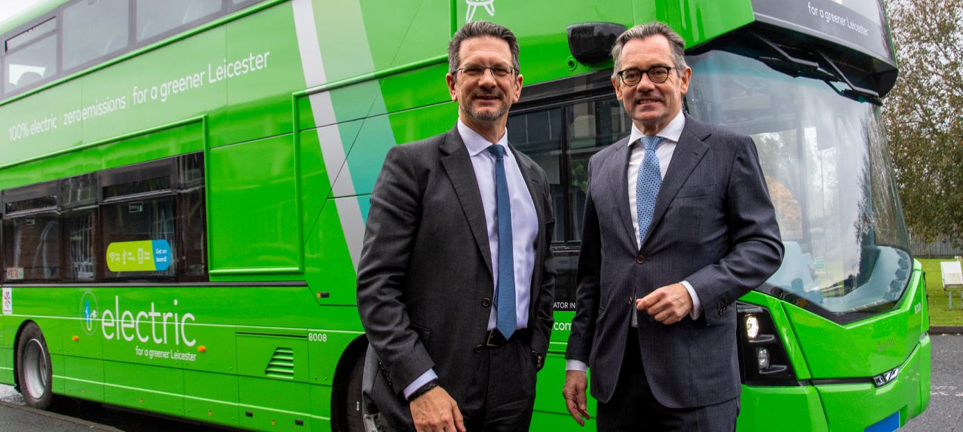 two men standing in front of a green double decker electric bus
