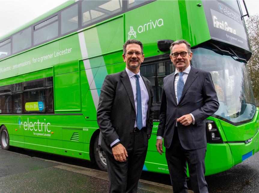 two men standing in front of a green double decker electric bus