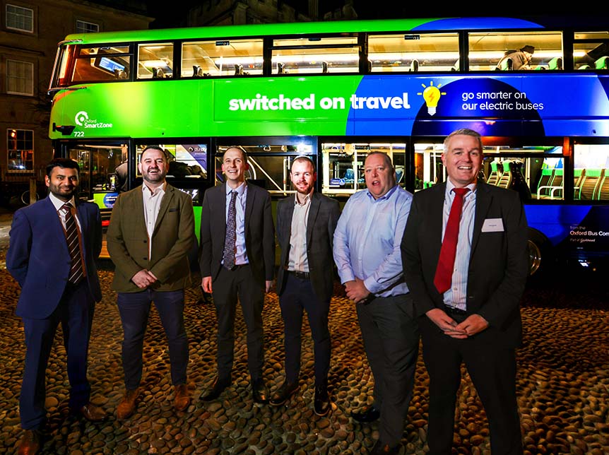 group of men standing in front of a double deck electric bus