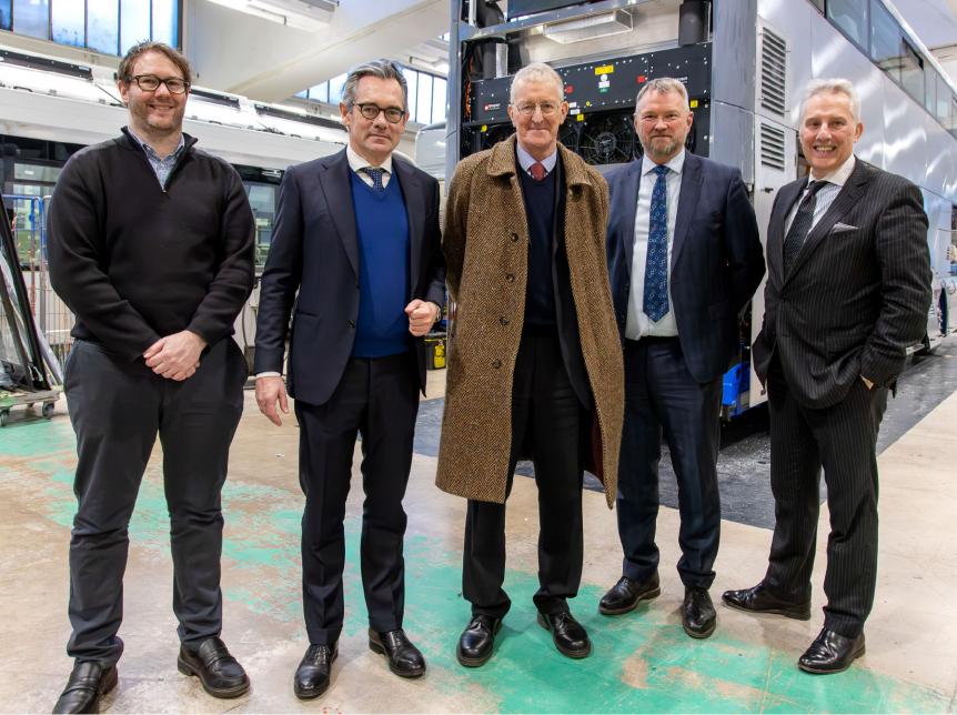 Group of men standing in a bus factory smiling at the camera