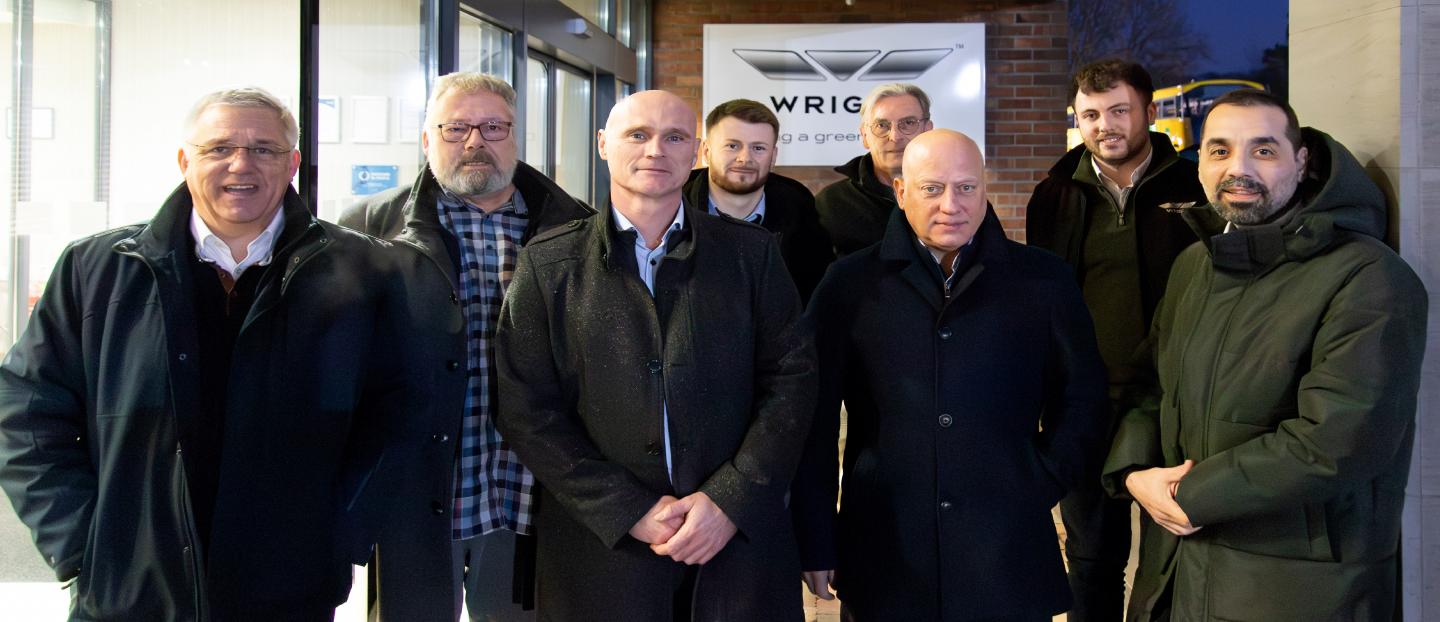 group of men standing in front of a factory entrance. a black and white sign in background reads 'Wrightbus'