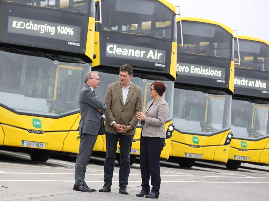 3 people talking in front of a row of parked yellow double deck buses