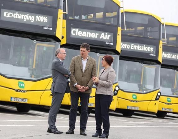 3 people talking in front of a row of parked yellow double deck buses