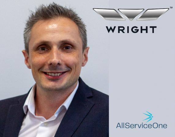Photo of Jon Eardley smiling at camera. he is wearing a white shirt and navy blazer. the background is grey. Wrightbus and AllServiceOne logos are on right hand side