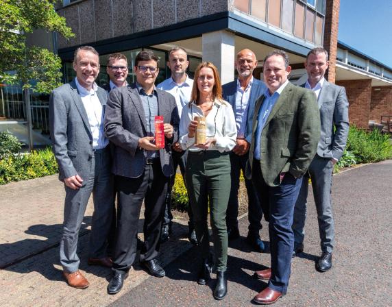 Members of the wrightbus senior team standing outside the factory. A lady in the centre of the photo is holding one award, the man beside her is holding the second award