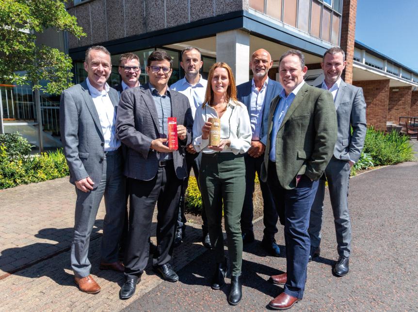 Members of the wrightbus senior team standing outside the factory. A lady in the centre of the photo is holding one award, the man beside her is holding the second award
