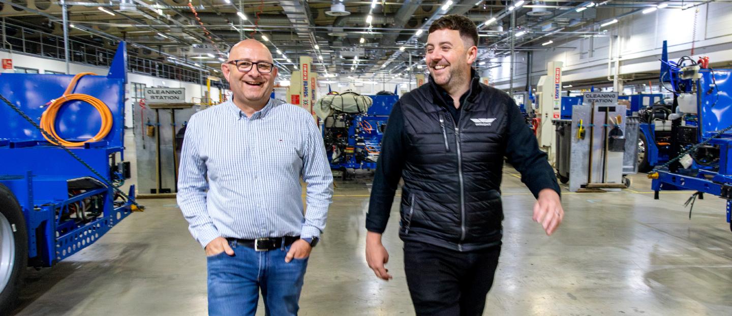 two men walking through a bus factory talking and laughing