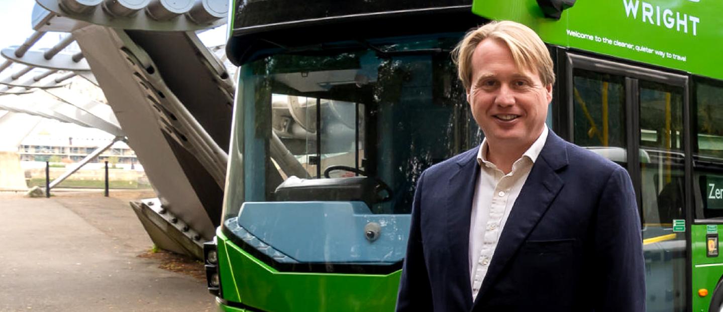 Jo Bamford CBE standing in front of a hydrogen double deck bus from Wrightbus