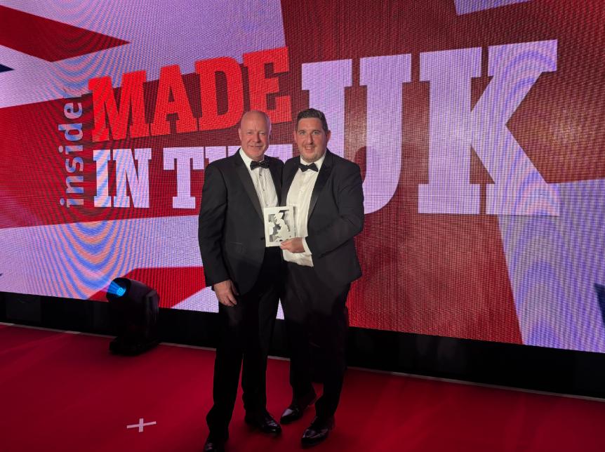 two men holding an award standing in front of a large led screen that reads "made in the UK"