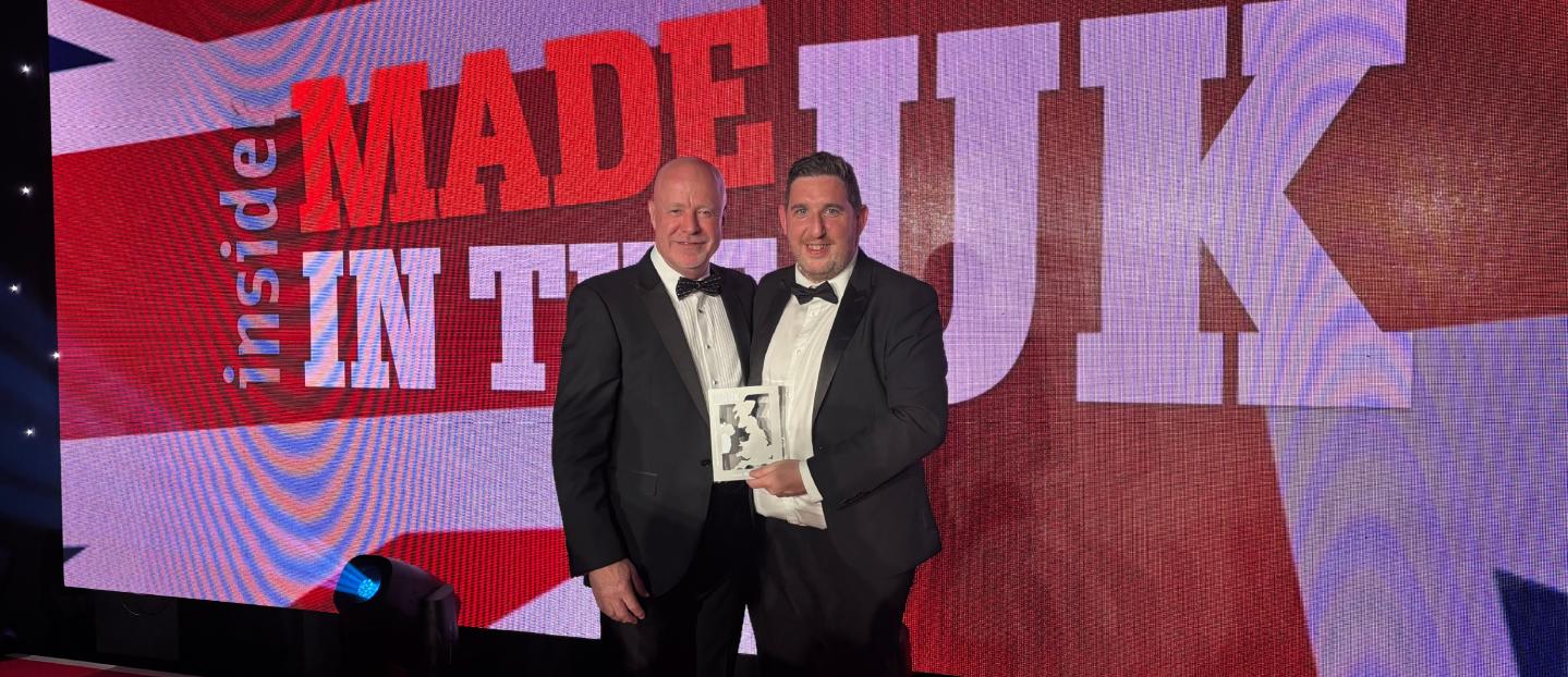two men holding an award standing in front of a large led screen that reads "made in the UK"