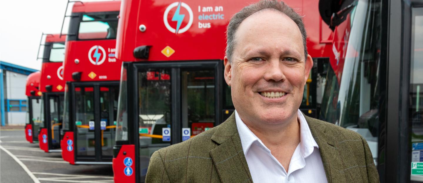 Paul Thomas standing in front of a line of red double deck buses. He is smiling at the camera