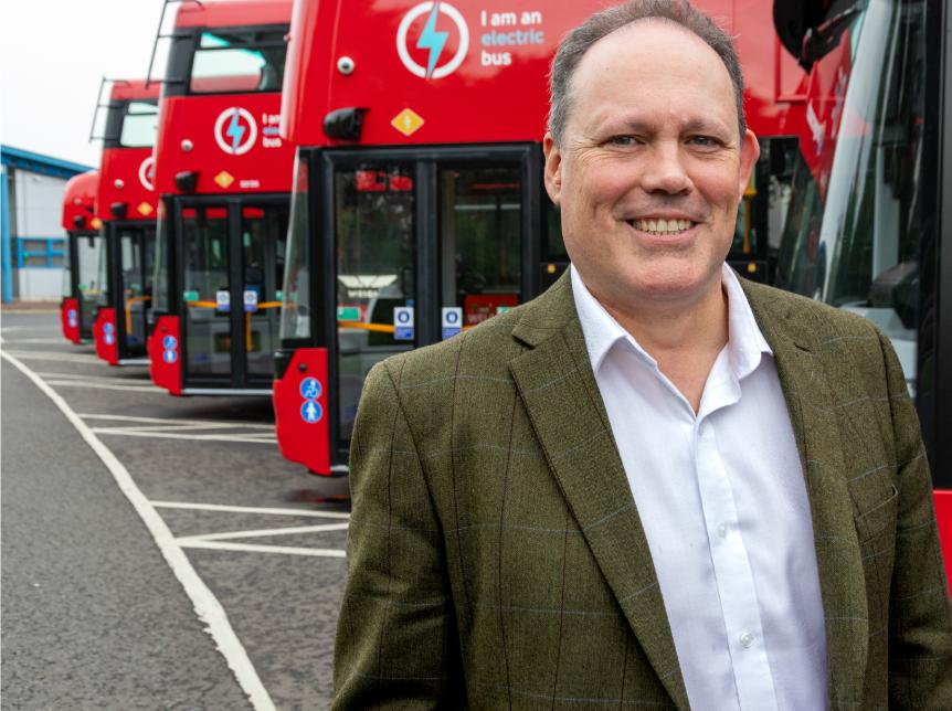 Paul Thomas standing in front of a line of red double deck buses. He is smiling at the camera