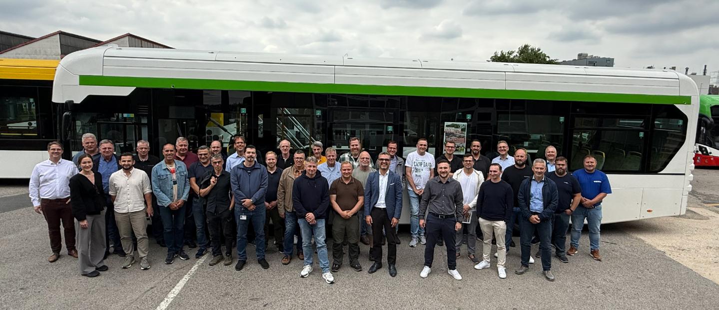 a large group of people standing in lines in front of a single deck hydrogen bus.