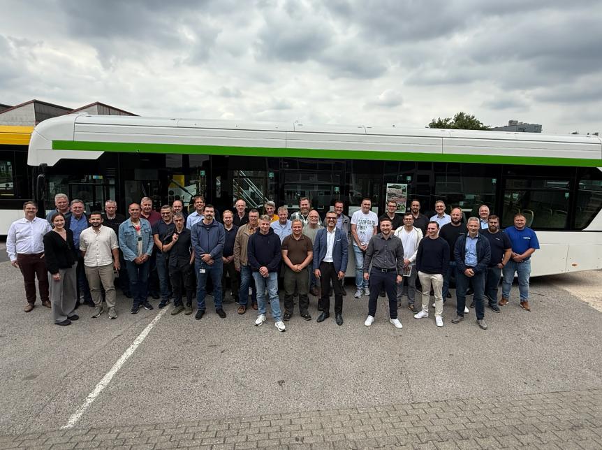 a large group of people standing in lines in front of a single deck hydrogen bus.