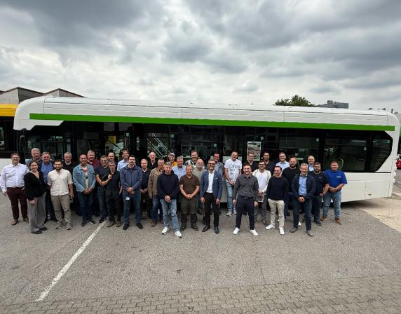 a large group of people standing in lines in front of a single deck hydrogen bus.