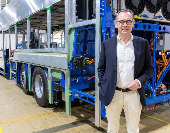 Jean-Marc Gales standing beside a bus chassis inside factory